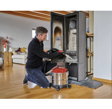 Een man reinigt een houtkachel met een aszuiger in een woonkamer.