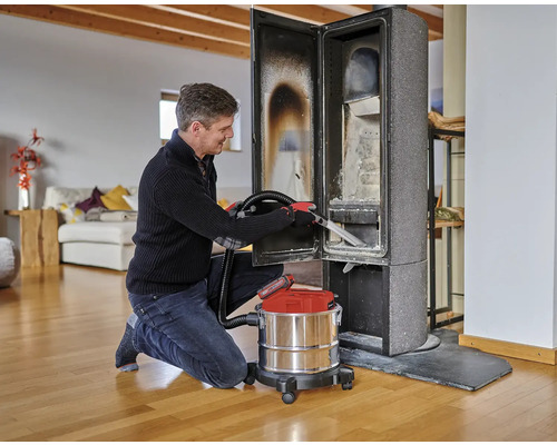 Een man reinigt een houtkachel met een aszuiger in een woonkamer.