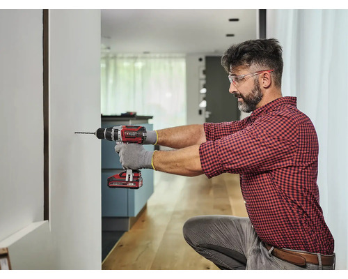 Man boort een gat in een muur met een accuboormachine.