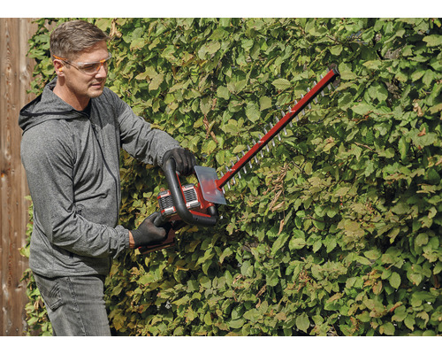 Een persoon snoeit een haag met een heggenschaar.