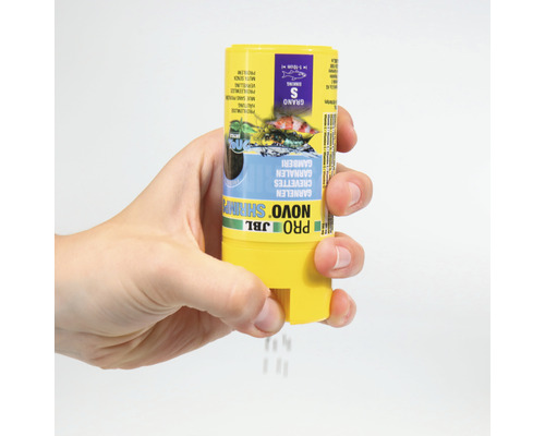 Hand houdt een pot JBL Novo Shrimp korrelvoer voor siergarnalen vast.