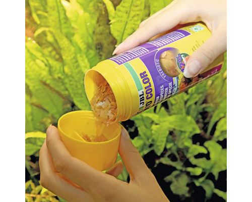 Een persoon giet JBL Novo Color vlokkenvoer in een maatbeker.