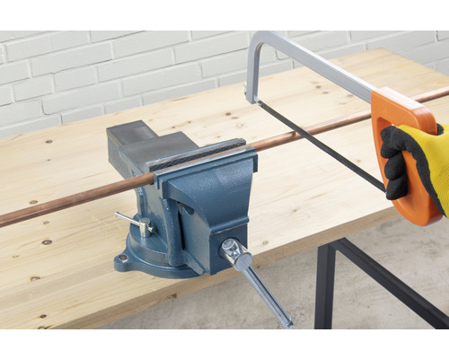 Een bankschroef houdt een koperen buis vast die wordt doorgesneden met een metaalzaag.