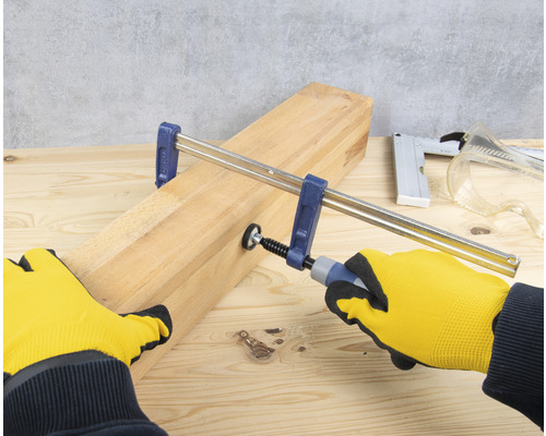 Aandraaien van een lijmklem op een houten plank met handschoenen