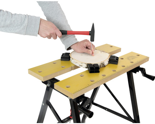 Persoon spijkert met een hamer een spijker in een stuk hout dat is bevestigd met een werkbank.