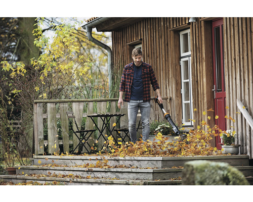 Man gebruikt een bladblazer op een houten terras om bladeren te verwijderen.