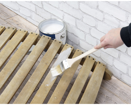 Een houten lattenconstructie wordt geschilderd met een kwast naast een verfemmer