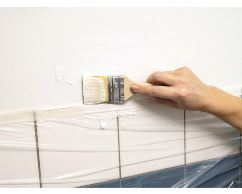 Een persoon schildert een muur boven tegels afgedekt met folie met een kwast.