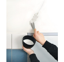 Iemand vult een scheur in de muur met een plamuurmes. Er wordt een bakje met vulmateriaal vastgehouden.