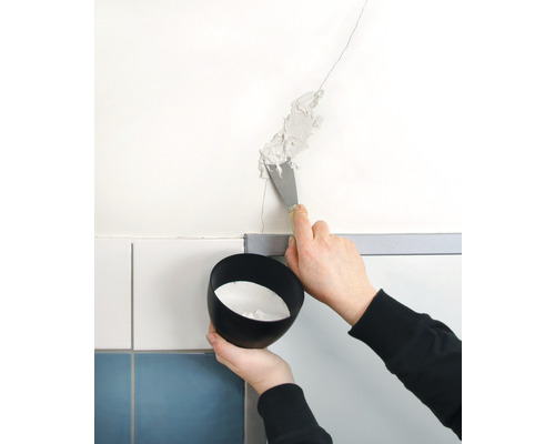 Iemand vult een scheur in de muur met een plamuurmes. Er wordt een bakje met vulmateriaal vastgehouden.