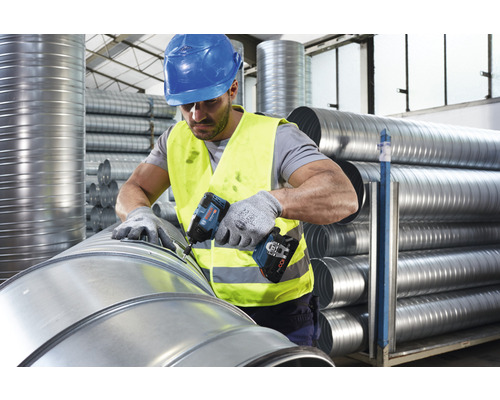 Een man in werkkleding gebruikt een accuschroefboormachine op een ventilatiepijp.