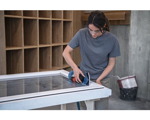 Vrouw schuurt raamkozijn met een excentrische schuurmachine