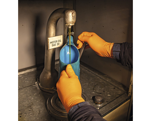 Een persoon met handschoenen vult motorolie SAE 30 in een container.
