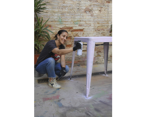 Vrouw spuit verf op een tafel buitenshuis.