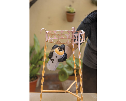 Een persoon spuit een metalen plantentrap met een spuitbus. De plantentrap heeft een spiraalvormig ontwerp.