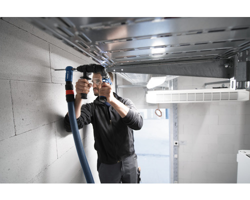 Man boort gat in de muur met boorhamer en stofafzuiging