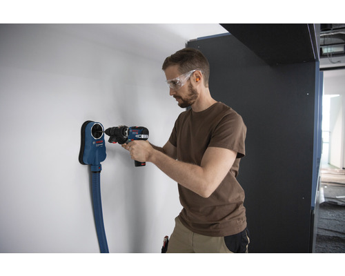 Een man boort met een accuschroefboormachine een gat in een muur, waarbij een stofafzuigapparaat van Bosch wordt gebruikt