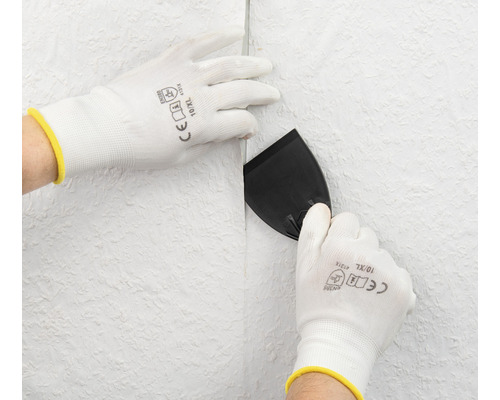 Persoon maakt behang glad met een plamuurmes en beschermende handschoenen