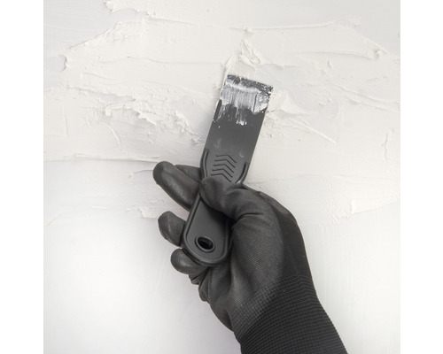Hand met handschoen en plamuurmes bij het pleisteren van een muur