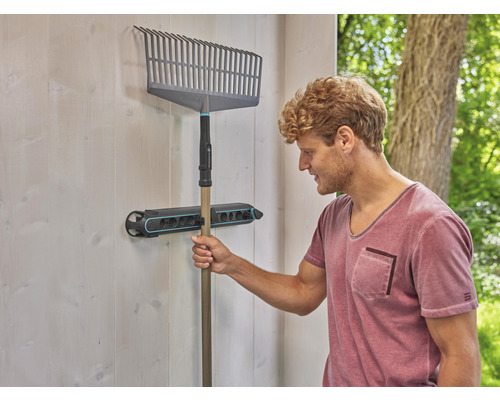 Een hark hangt aan een gereedschaphouder aan de muur.