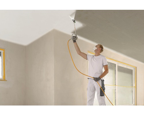 Een man gebruikt een verfspuit om een plafond te schilderen tijdens een kamerrenovatie.