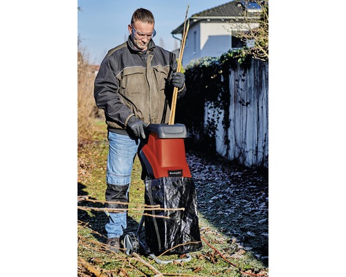 Een persoon gebruikt een hakselaar in de tuin om takken en twijgen te versnipperen.
