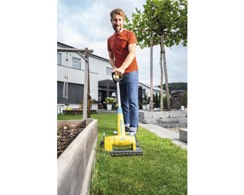 Man gebruikt een gele gazonbeluchter in de tuin.