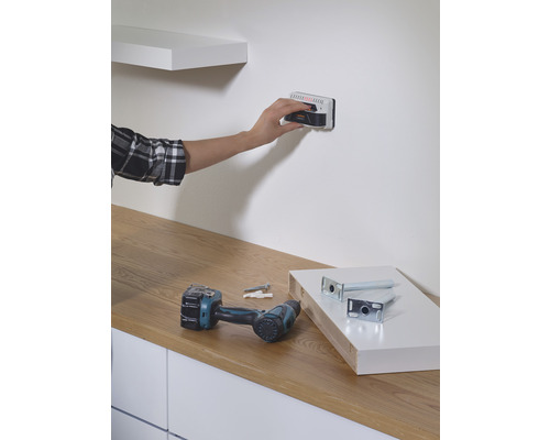 Persoon gebruikt wandscanner om een plank aan de muur te bevestigen