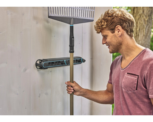 Man hangt een hark in een gereedschaphouder aan een wand