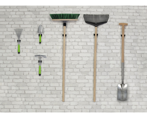 Diverse tuingereedschappen zoals harken, schep en bezem hangen aan een muur.
