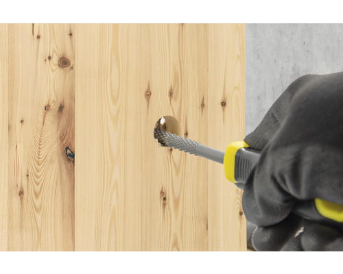 Een persoon vergroot met een houtrasp een gat in een houten plank.