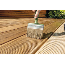 Een persoon schildert een houten terras met een platte kwast.