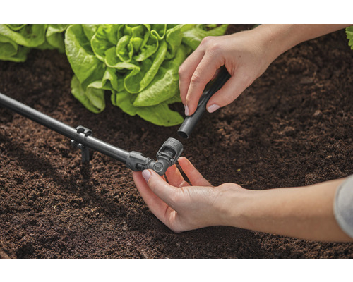 Tuinscene met irrigatiesysteem en een persoon die een verbindingsstuk bevestigt.