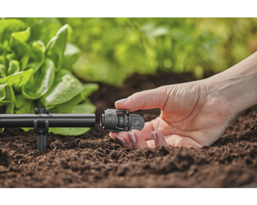 Gedetailleerde opname van een persoon die een connector aan een irrigatiesysteem in de tuin bevestigt