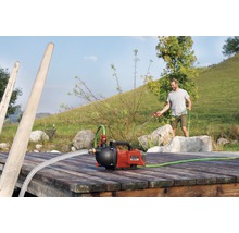 Einhell hydrofoorpomp op een houten steiger met een man op de achtergrond die water geeft met een tuinslang