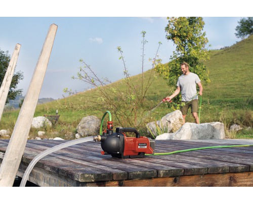 Einhell hydrofoorpomp op een houten steiger met een man op de achtergrond die water geeft met een tuinslang