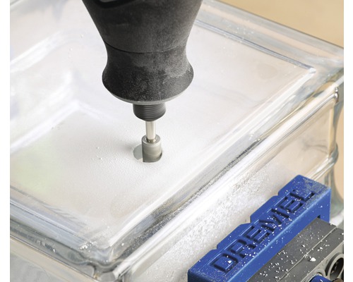 Een gereedschap boort een gat in een glazen bouwsteen die in een bankschroef is bevestigd