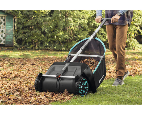 Een persoon gebruikt een Gardena bladveger in de tuin om herfstbladeren te verzamelen.