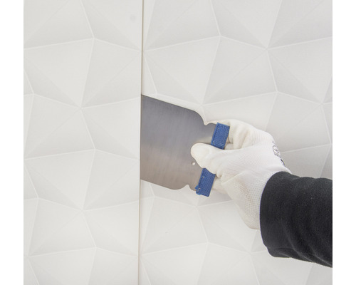 Een hand met handschoen strijkt behang glad met een spatel.