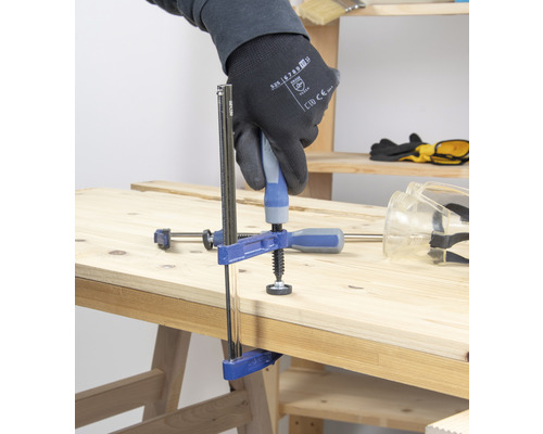 Een lijmklem fixeert twee stukken hout op een werkbank.