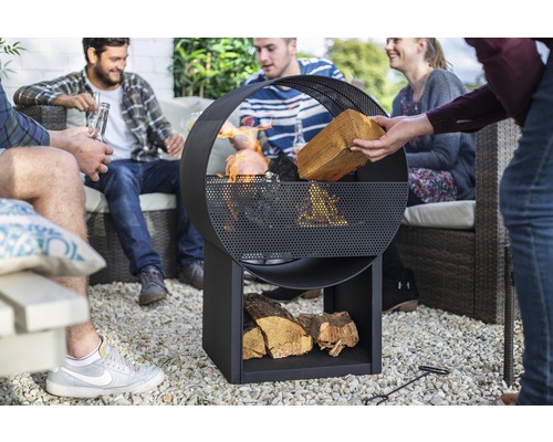 Groep mensen zit rond een metalen vuurplaats met houtopslag in de tuin.