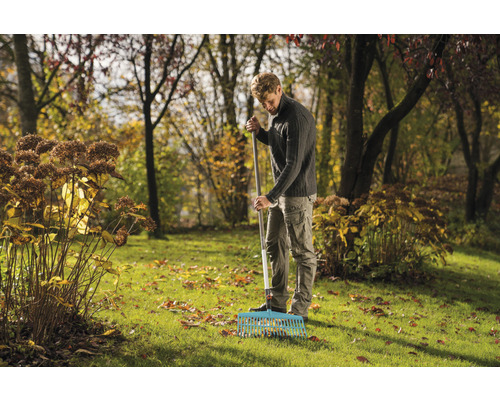 Een man harkt bladeren in een tuin met een hark.