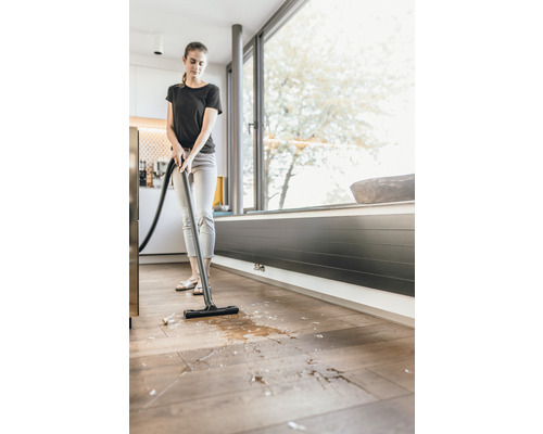 Vrouw zuigt vloeistoffen en vuil op met een nat- en droogzuiger van de houten vloer.