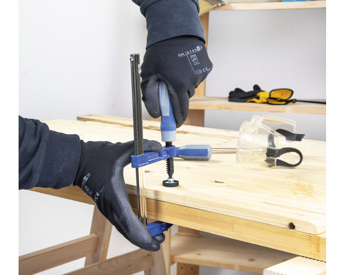 Iemand bevestigt twee houten planken met een eenhandsklem op een werkbank.