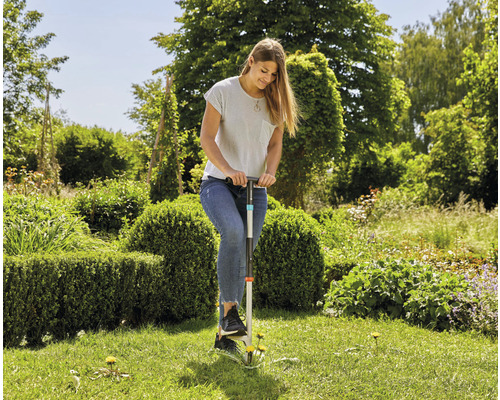 Een vrouw verwijdert onkruid met een onkruidsteker in de tuin.