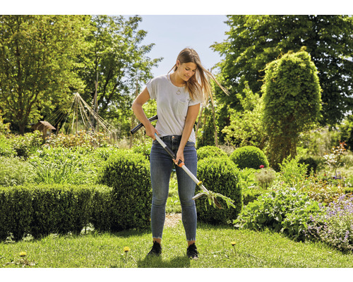 Vrouw gebruikt een onkruidsteker in de tuin.