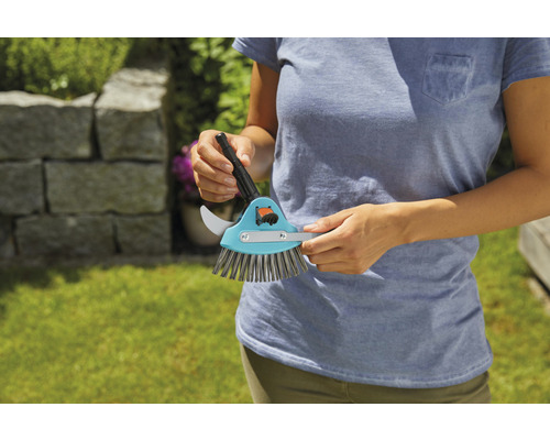 Een persoon houdt een voegenkrabberborstel vast met voegenkrabber en borstel.