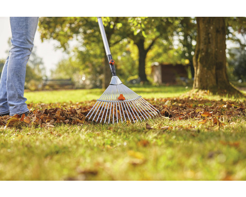 Iemand harkt bladeren met een bladhark in de tuin.