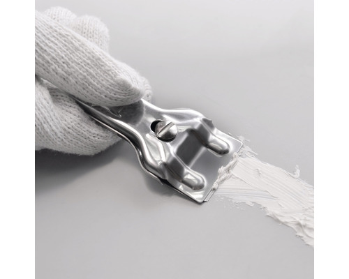 Een hand met een witte handschoen houdt een metalen plamuurmes vast dat plamuur op een oppervlak verdeelt.