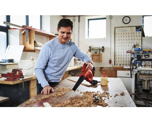 Een man gebruikt een accu bladblazer om een werkbank schoon te maken van houtsnippers in een werkplaats.